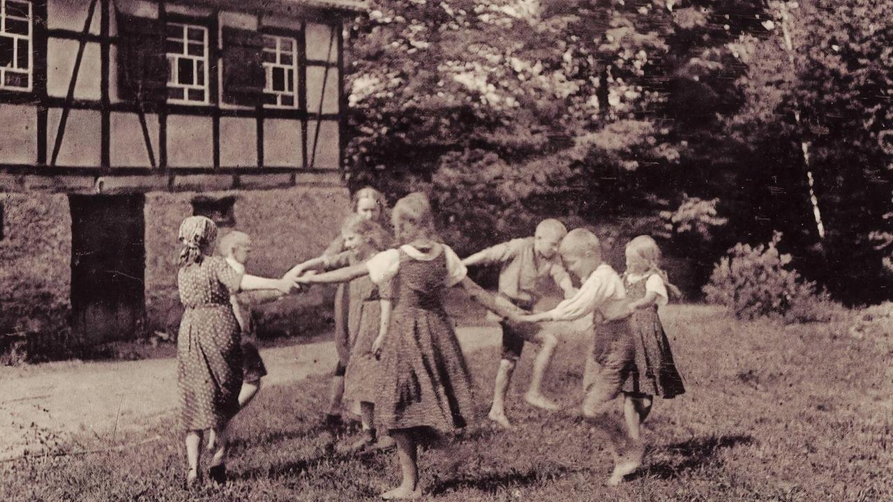 Eine historische Aufnahme zeigt Kinder, die sich tanzend an den Händen fassen, vor einem Landheim der Wandervögel in Döbeln in Sachsen 1915.