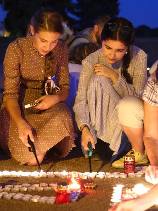 Junge Frauen knien auf dem Marsfeld in St. Petersburg und zünden Kerzen zum Gedenken an den Überfall der Deutschen auf die Sowjetunion 1941 an.