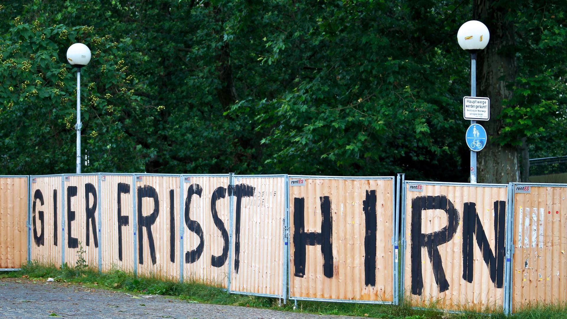 Auf einem Bauzaun ist in großen Buchstaben "Gier frisst Hirn" geschrieben. Auf einem Bauzaun ist in großen Buchstaben "Gier frisst Hirn" geschrieben.