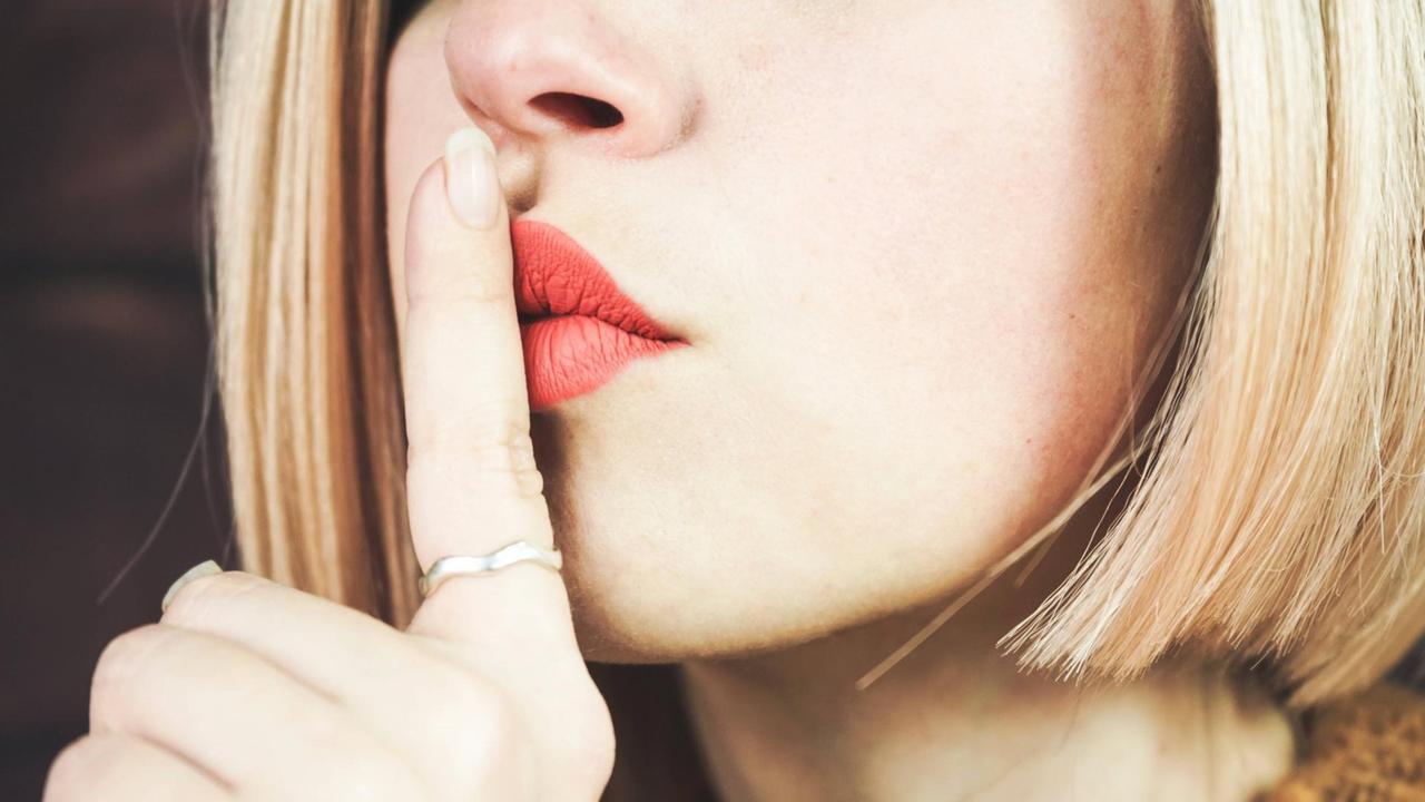 Eine blonde junge Frau legt ihren Zeigefinger auf die Lippen und symbolisiert Schweigen. Eine blonde junge Frau legt ihren Zeigefinger auf die Lippen und symbolisiert Schweigen.