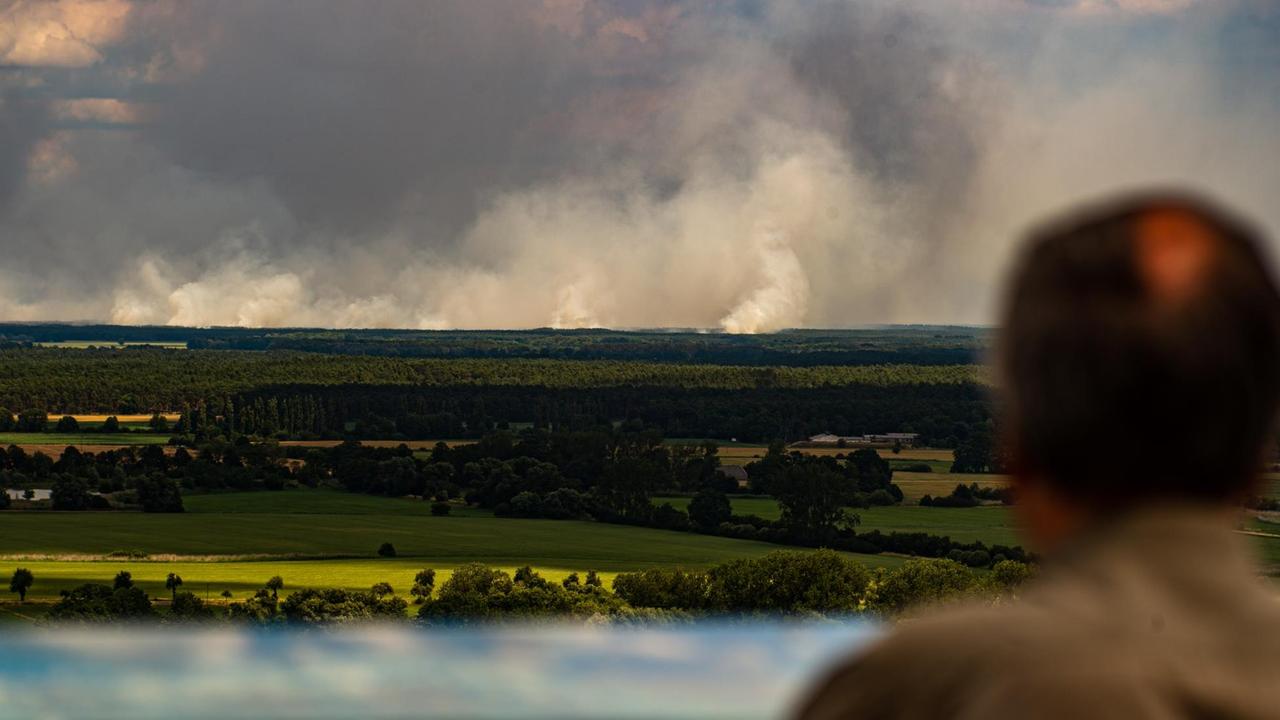 01.07.2019, Niedersachsen, Drehtem: Ein Mann blickt von einem Aussichtsturm von Niedersachsen aus über die Elbe auf den Waldbrand auf den Waldbrand bei Lübtheen in Mecklenburg-Vorpommern. Wegen des Waldbrandes auf dem ehemaligen Truppenübungsplatz bei Lübtheen in Mecklenburg-Vorpommern mussten Hunderte Menschen ihre Wohnungen verlassen. 01.07.2019, Niedersachsen, Drehtem: Ein Mann blickt von einem Aussichtsturm von Niedersachsen aus über die Elbe auf den Waldbrand auf den Waldbrand bei Lübtheen in Mecklenburg-Vorpommern. Wegen des Waldbrandes auf dem ehemaligen Truppenübungsplatz bei Lübtheen in Mecklenburg-Vorpommern mussten Hunderte Menschen ihre Wohnungen verlassen.
