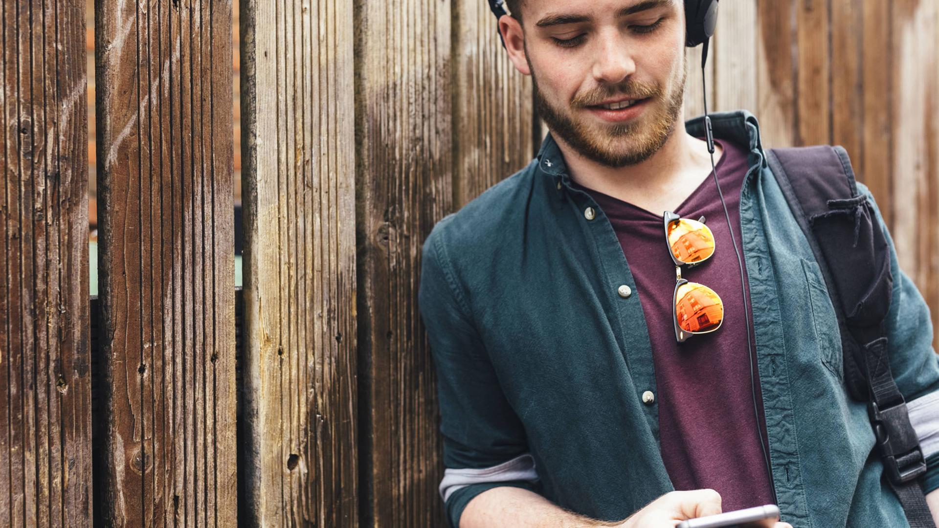 Ein junger Mann mit Kopfhörern scrollt auf seinem Smartphone. Ein junger Mann mit Kopfhörern scrollt auf seinem Smartphone.