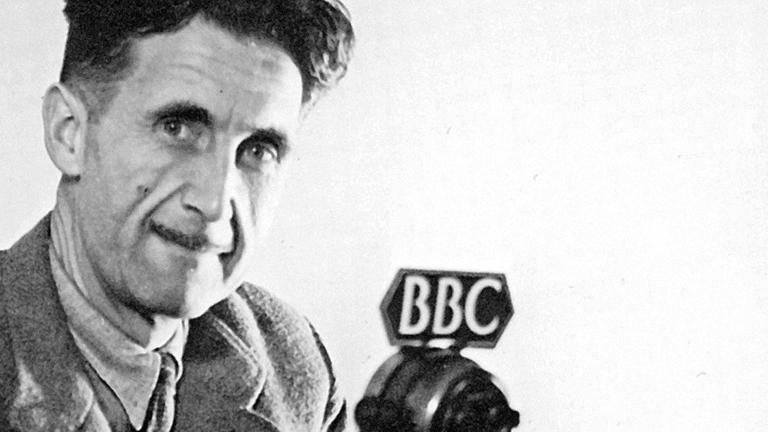 George Orwell sitzt an einem Mikrofon der BBC und blickt in die Kamera.