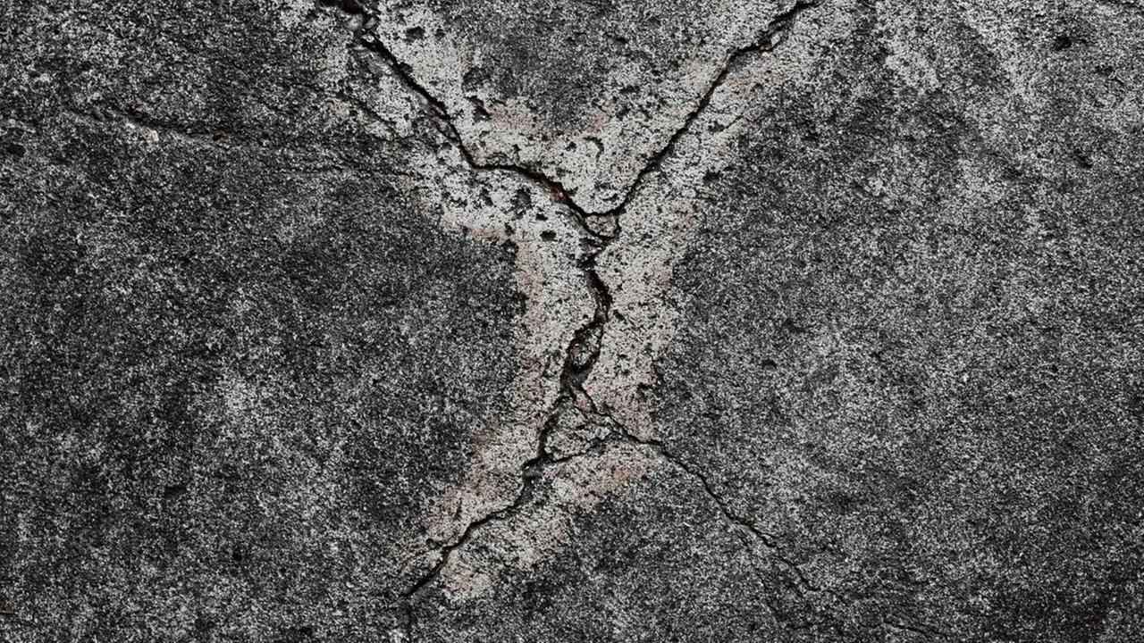 Eine Nahaufnahme zeigt rissigen Beton. Eine Nahaufnahme zeigt rissigen Beton.