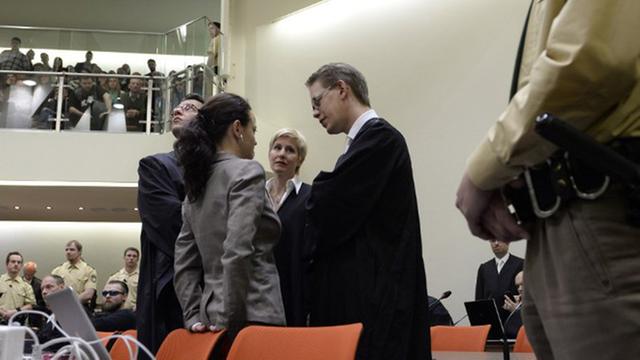 Beate Zschäpe steht im Münchner Gerichtssaal an einen Stuhl gelehnt, umringt von ihren Anwälten.