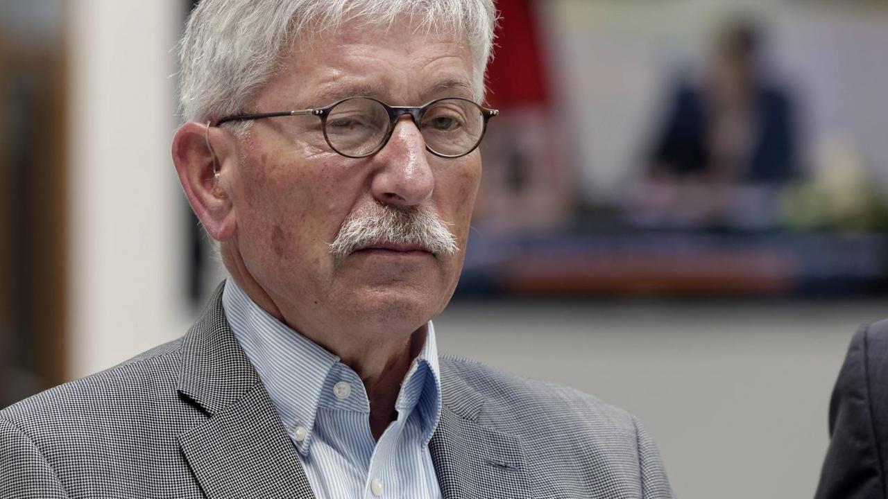 Sarrazin trägt einen grauen Anzug und ein weißes Hemd. Sarrazin trägt einen grauen Anzug und ein weißes Hemd.