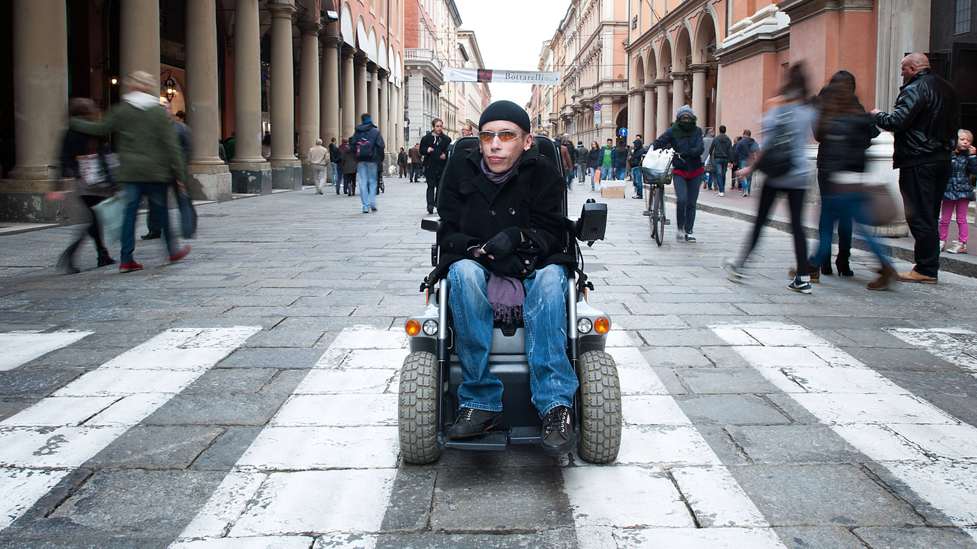 Der an Muskeldystrophie erkrankte Maximiliano Ulivieri in Bologna. Ulivieri sitzt im Rollstuhl in einer Fußgängerstraße. Der an Muskeldystrophie erkrankte Maximiliano Ulivieri in Bologna. Ulivieri sitzt im Rollstuhl in einer Fußgängerstraße.