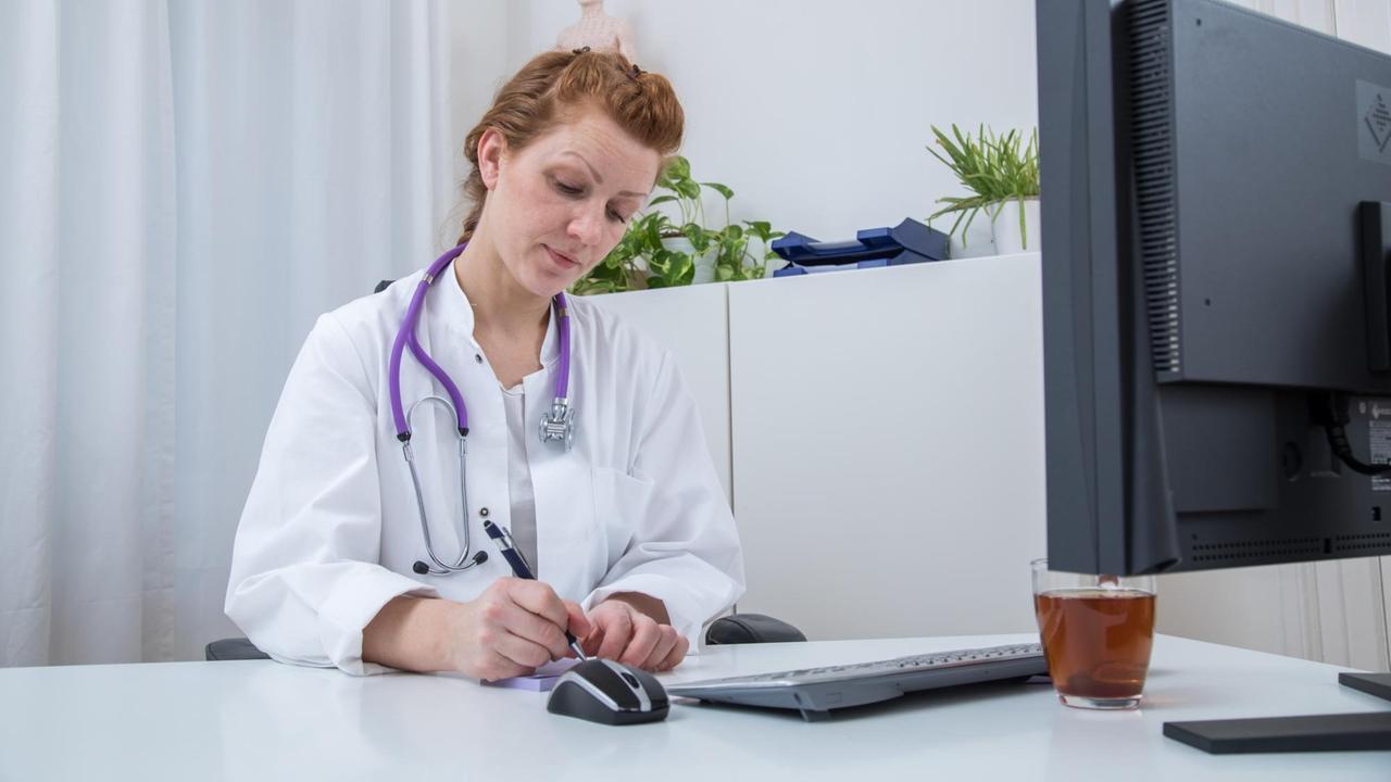 Eine junge Ärztin sitzt an ihrem Schreibtisch und schreibt auf einem Notizblock. 