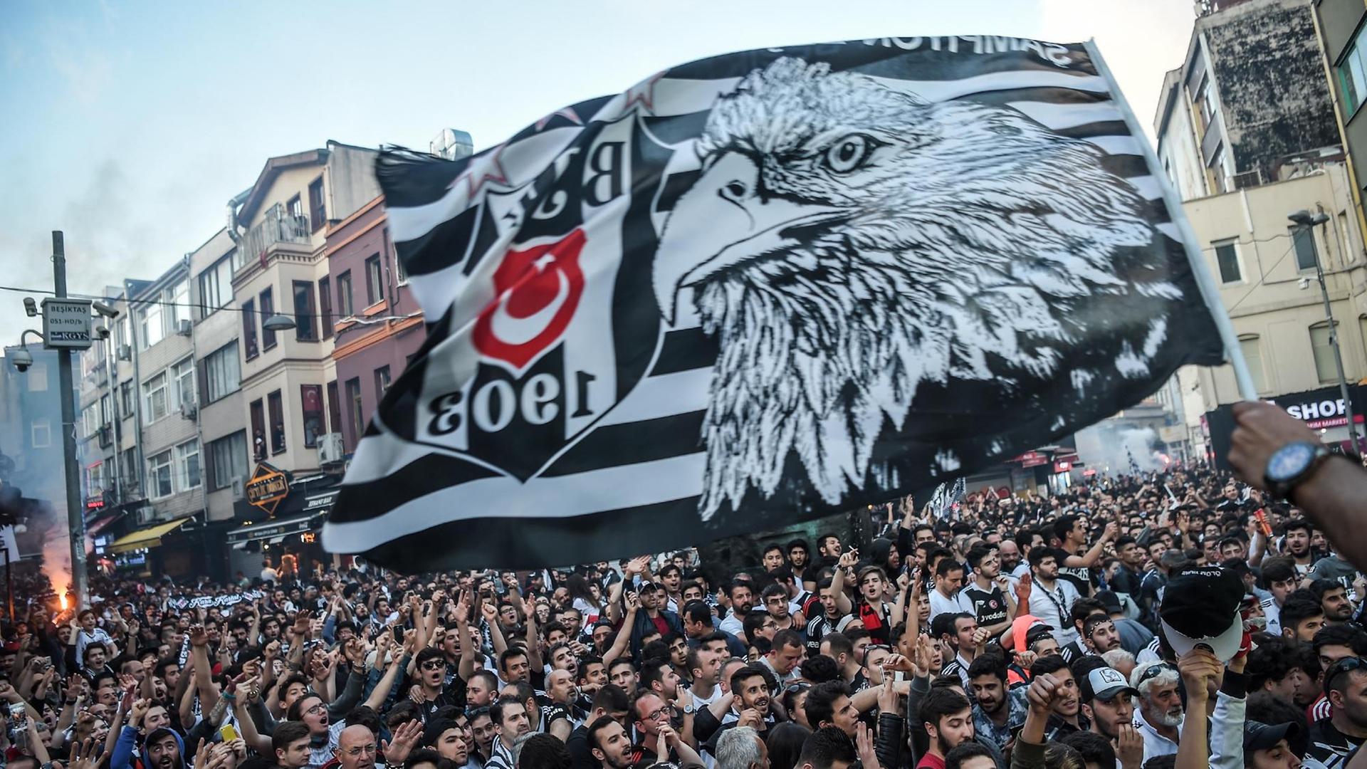 Fans von Besiktas Istanbul feiern den vorzeitigen Gewinn der Meisterschaft ihres Vereins. Ein Mann schwenkt vor einer Menschenmenge eine große schwarze Fahne mit Adler-Kopf Fans von Besiktas Istanbul feiern den vorzeitigen Gewinn der Meisterschaft ihres Vereins. Ein Mann schwenkt vor einer Menschenmenge eine große schwarze Fahne mit Adler-Kopf