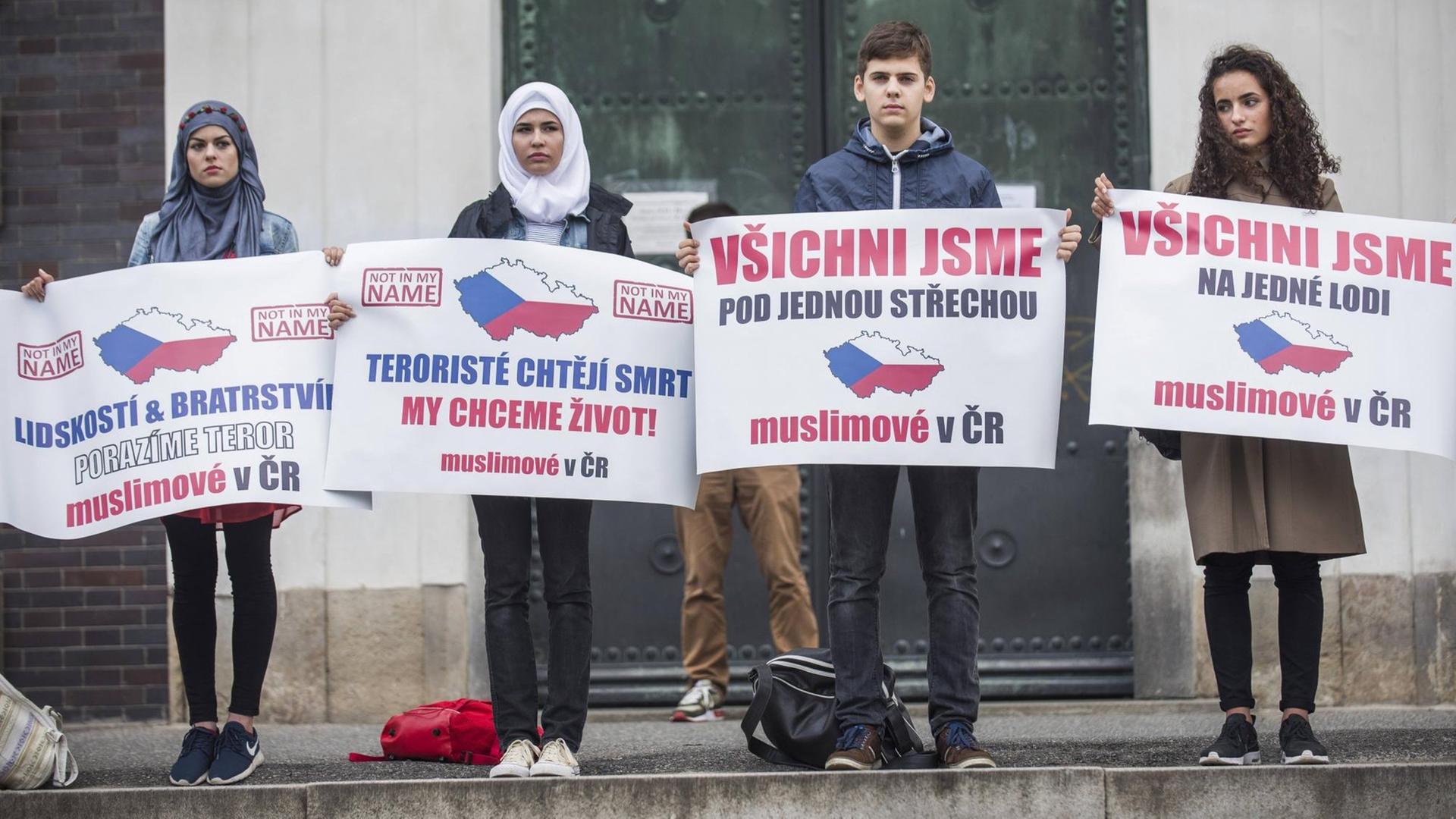 Vier muslimische Demonstranten stehen mit Plakaten vor einer katholischen Kirche in Prag.
