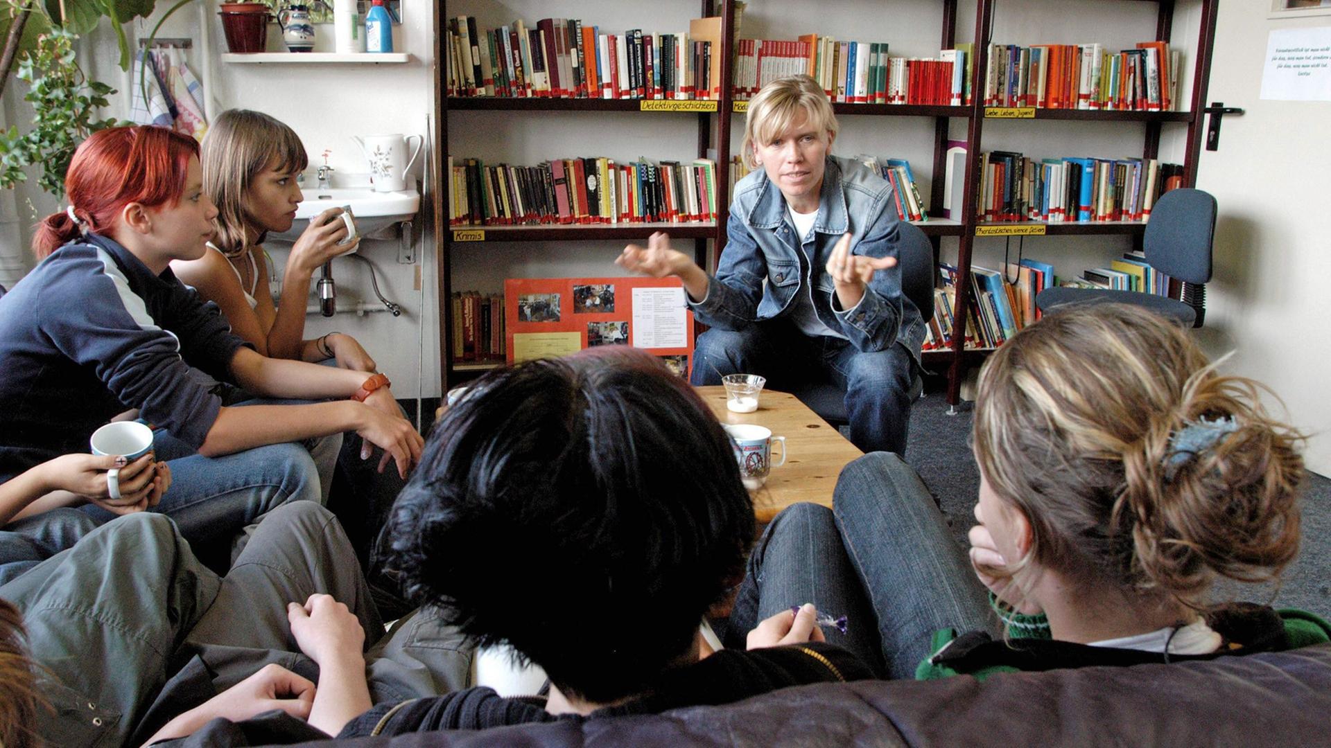 Eine Sozialarbeiterin diskutiert mit Schülerinnen, die auf einem Sofa sitzen.