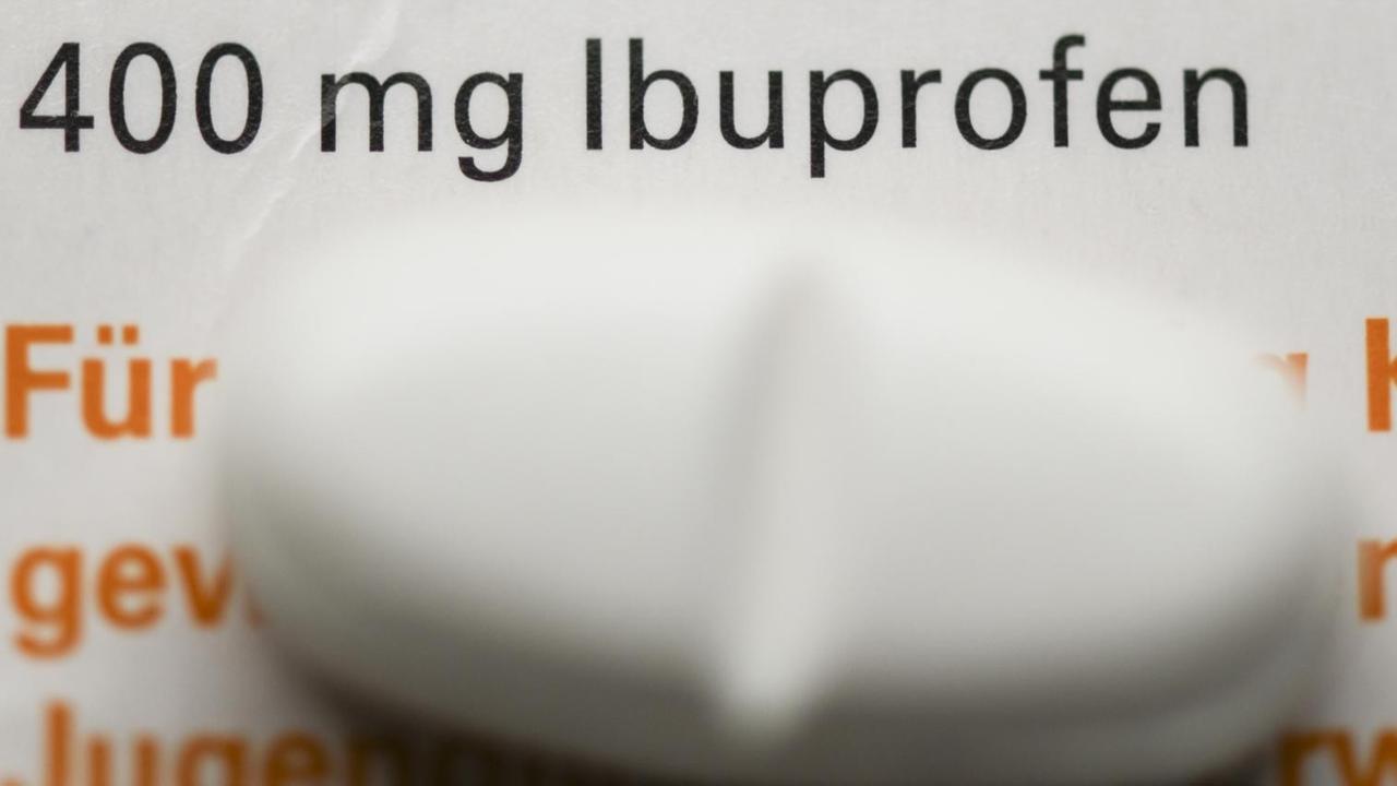 Eine Tablette mit dem Wirkstoff Ibuprofen liegt auf einer Medikamentenschachtel. 