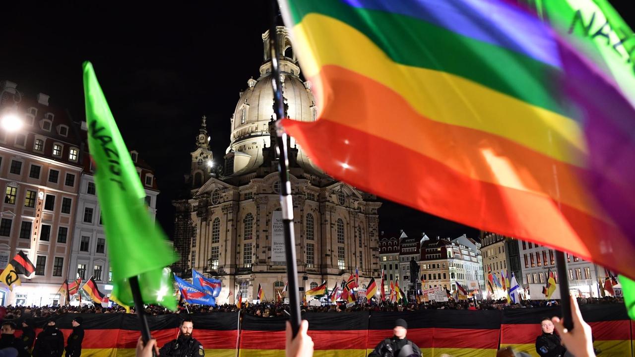 Pegida-Demonstranten schwenken vor der Frauenkirche auf dem Dresdner Neumarkt Flaggen, während im Vordergrund Gegendemonstranten stehen und ebenfalls Flaggen schwenken. Pegida-Demonstranten schwenken vor der Frauenkirche auf dem Dresdner Neumarkt Flaggen, während im Vordergrund Gegendemonstranten stehen und ebenfalls Flaggen schwenken.