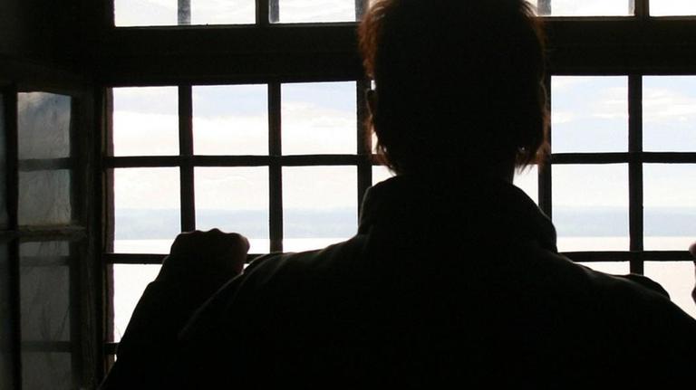 Ein Mann im Gefängnis vor einem vergitterten Fenster Ein Mann im Gefängnis vor einem vergitterten Fenster