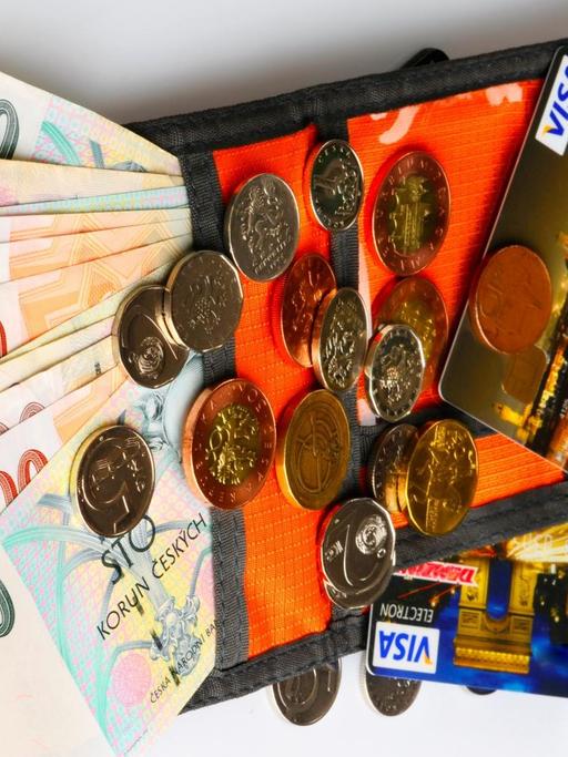 Eine orangefarbige Geldbörse mit tschechischen Kronen in Münzen und Scheinen ausgebreitet
