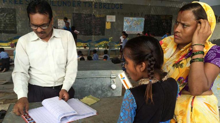 Geeta, im gelben Sari, meldet ihre kleine Tochter in der freien Schule unter der Metrobrücke im Osten Neu-Delhis an.