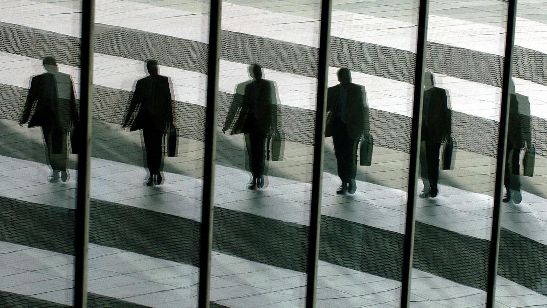 Ein Mann mit Aktentasche geht ins Büro und spiegelt sich dabei in den Glasscheiben. Ein Mann mit Aktentasche geht ins Büro und spiegelt sich dabei in den Glasscheiben.