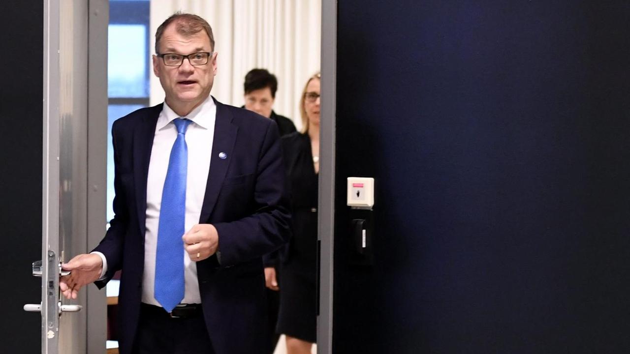Der Ministerpräsident von Finnland, Juha Sipilä - mit azurblauer Krawatte und Jacket -, öffnet die Tür in einen Konferenzraum. 