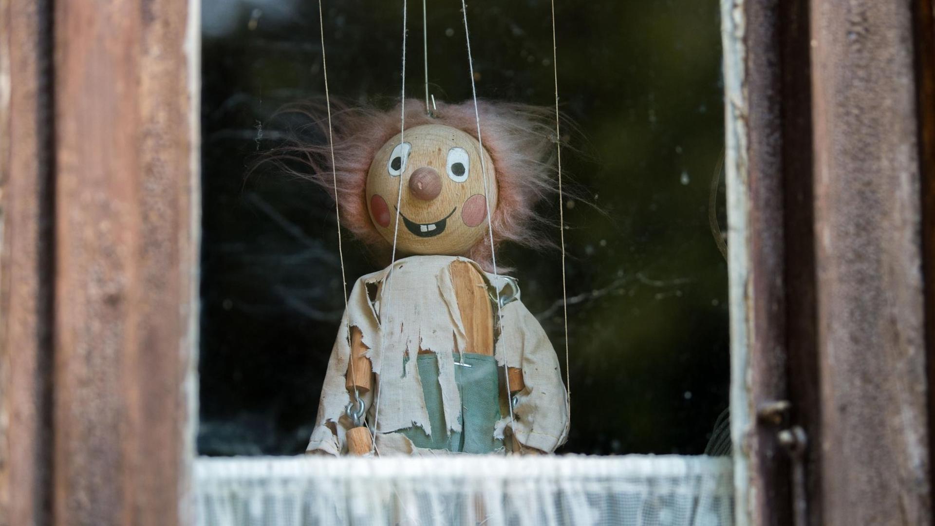 Marionette mit zerzaustem Haar und zerrissenen Klamotten in einem Fenster.