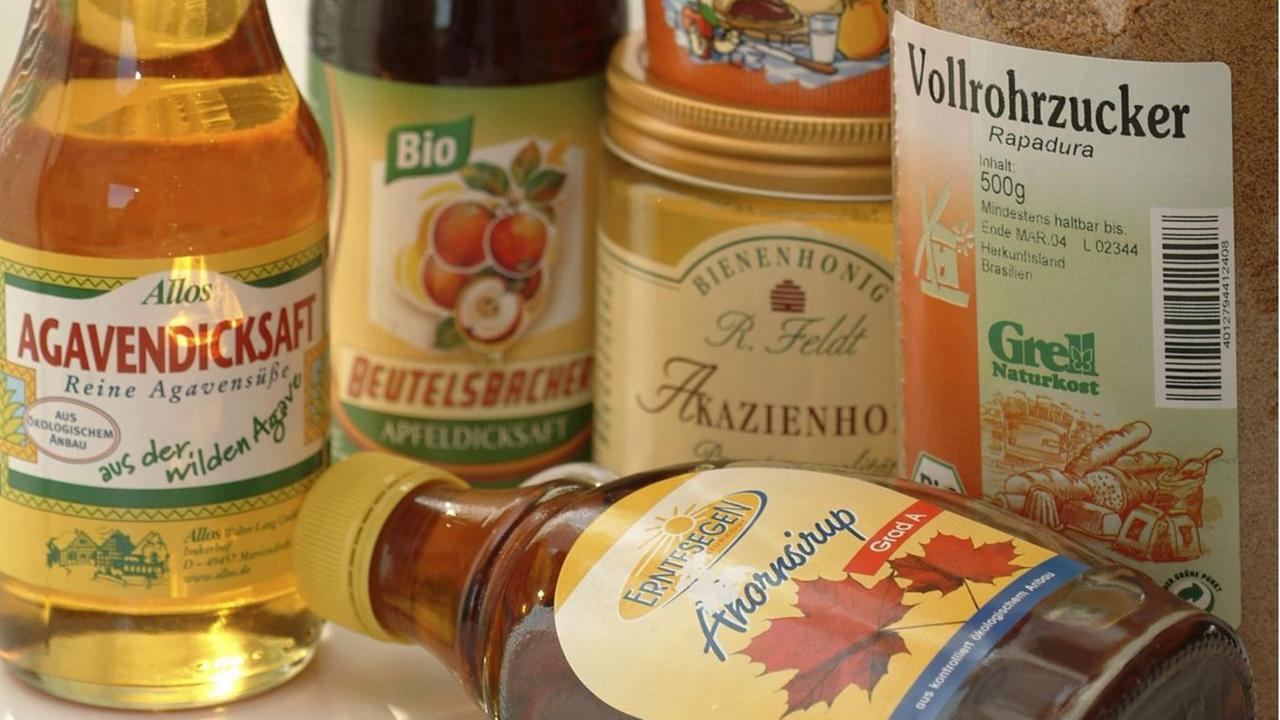 Alternative Süßungsmittel wie Ahornsirup, Agavendicksaft und Honig stehen zusammen auf einem Tisch