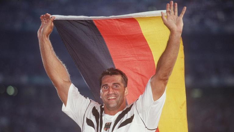 Diskuswerfer Lars Riedel, Gewinner der Goldmedaille, jubelt mit einer deutschen Flagge