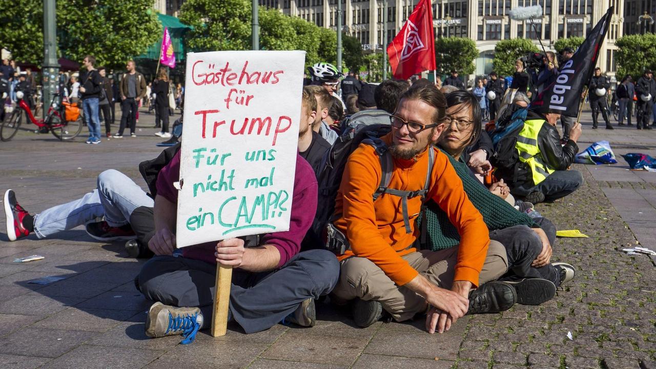 Demonstranten mit Papierschild sitzen auf dem Rathausplatz in Hamburg