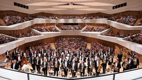 Ein Orchester steht vor einem voll besetzten Konzerthaus.