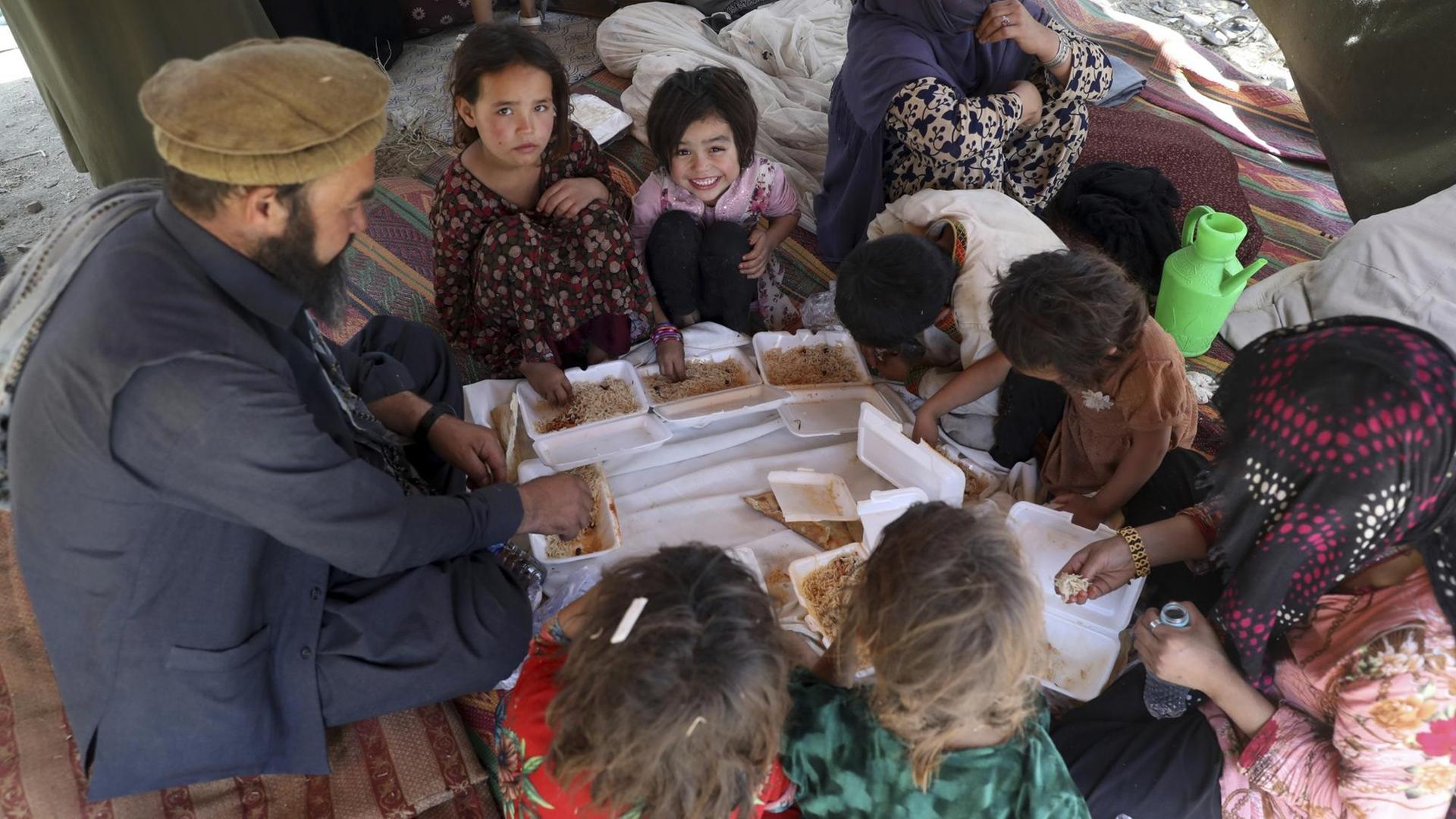  Von oben fotografierte Afghanen, Kinder und Erwachsene, sitzen um einen provisorischen Tisch und essen Lebensmittelspenden.