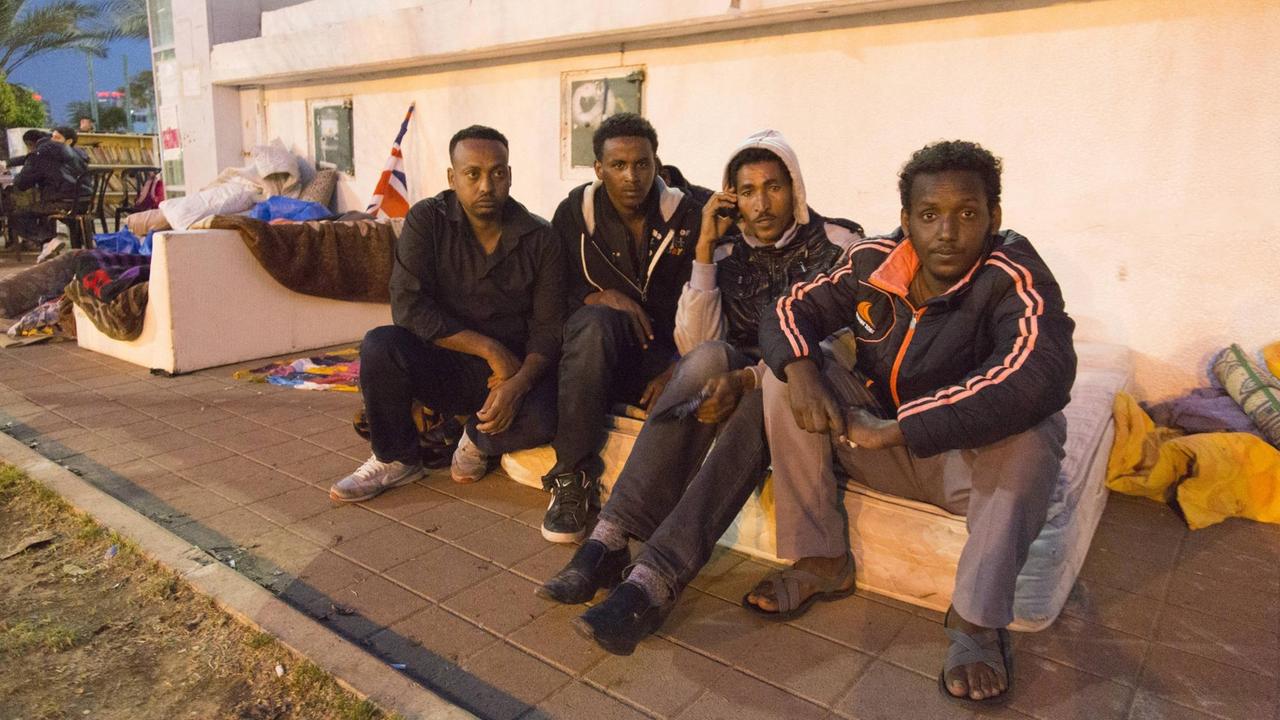 Vier schwarze Männer sitzen auf einer kleinen Mauer.