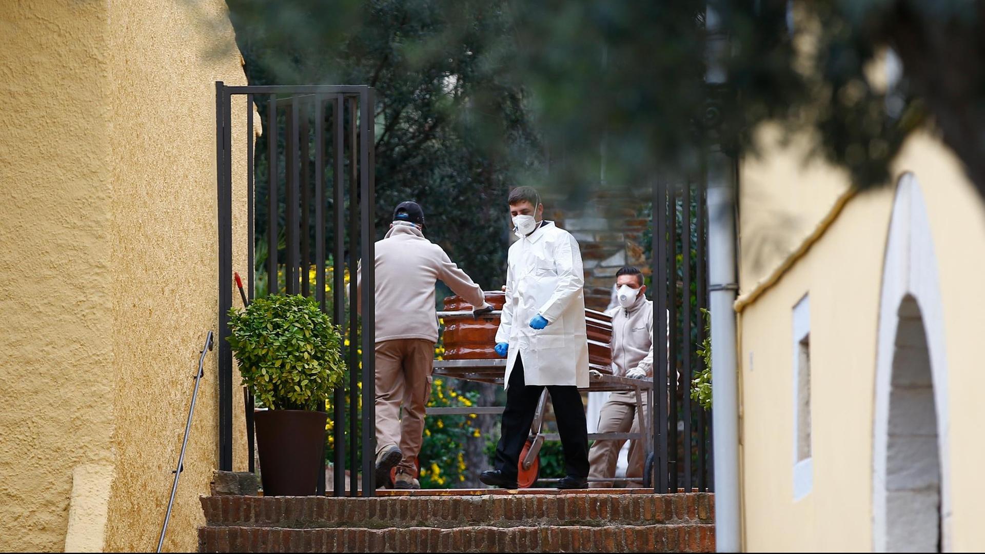 Bestatter in Schutzkleidung tragen aus einem Haus in Barcelona einen Sarg mit einem Menschen, der an Covid-19 gestorben ist. Bestatter in Schutzkleidung tragen aus einem Haus in Barcelona einen Sarg mit einem Menschen, der an Covid-19 gestorben ist.