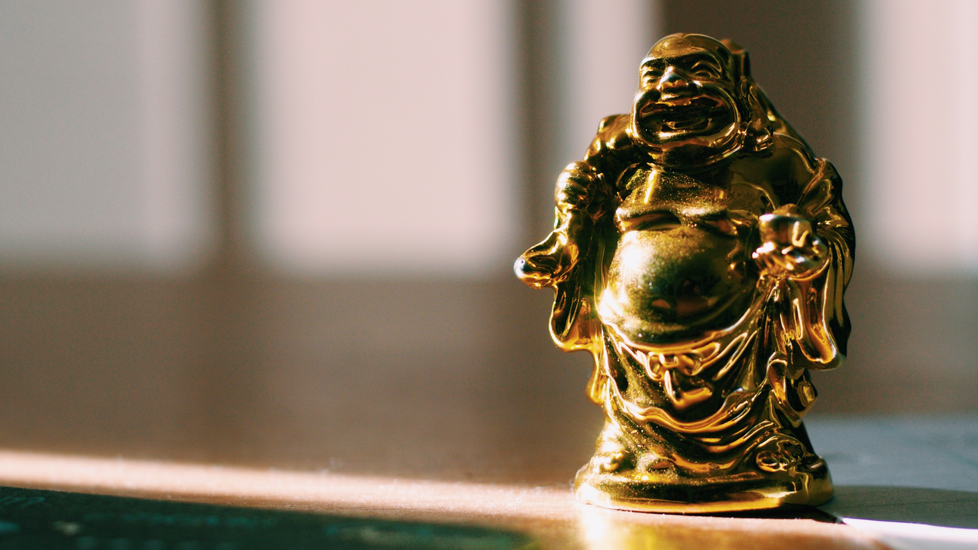 Eine kleine goldfarbene Statue eines lachenden Mönches wird von einem Sonnenstrahl angeleuchtet. Eine kleine goldfarbene Statue eines lachenden Mönches wird von einem Sonnenstrahl angeleuchtet.