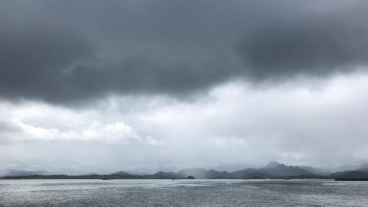 Vom Wasser aus ist eine Insel mit wolkenverhangenen Hügeln fotografiert. Vom Wasser aus ist eine Insel mit wolkenverhangenen Hügeln fotografiert.