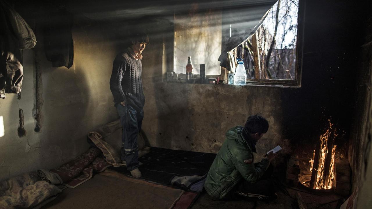 Zwei Afghanen wärmen sich an einem Feuer in einer verlassenen Fabrik.