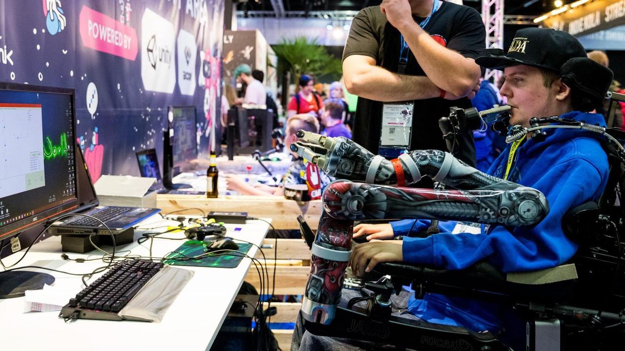 In einer Messehalle sitzt ein junger Mann vor einem Bildschirm und demonstriert mit einer speziellen Konstruktion, wie barrierefreies Computer spielen funktioniert. Es ist Dennis Winkens auf der Computerspielemesse Gamescom. In einer Messehalle sitzt ein junger Mann vor einem Bildschirm und demonstriert mit einer speziellen Konstruktion, wie barrierefreies Computer spielen funktioniert. Es ist Dennis Winkens auf der Computerspielemesse Gamescom.