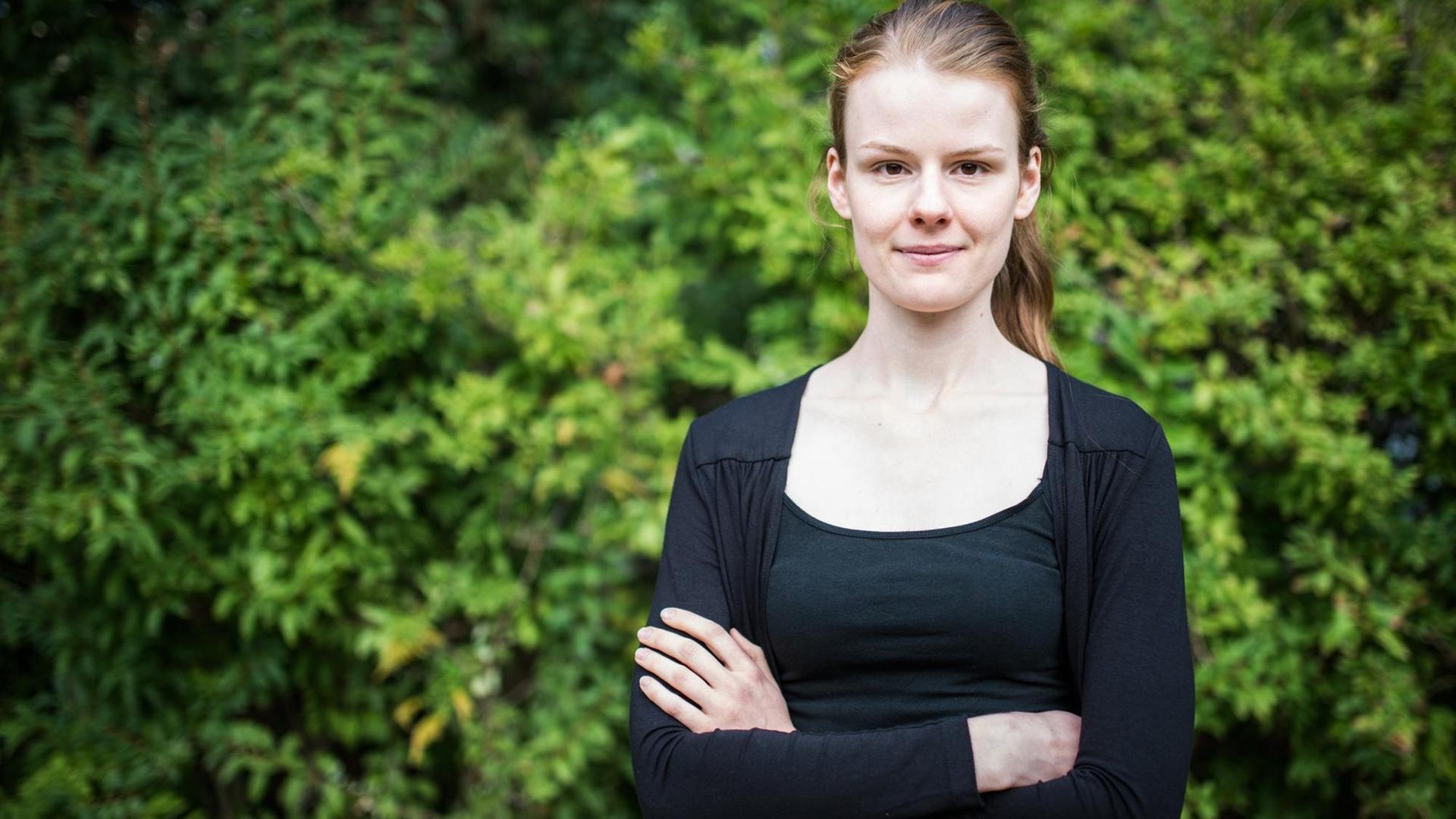 Eine junge, rothaarige Frau steht in schwarzer Kleidung mit verschränkten Armen vor einer grünen Hecke und schaut in die Kamera. Es ist die Berliner CDU-Politikerin Jenna Behrends. Eine junge, rothaarige Frau steht in schwarzer Kleidung mit verschränkten Armen vor einer grünen Hecke und schaut in die Kamera. Es ist die Berliner CDU-Politikerin Jenna Behrends.