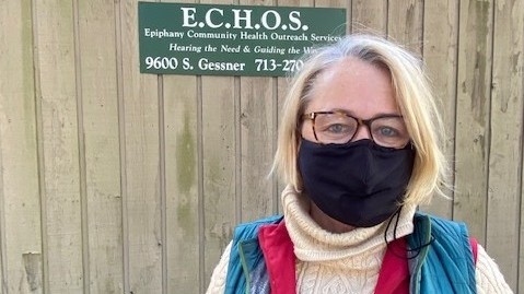 Eine blonde Frau mit Brille und schwarzem Mundschutz steht vor einem Schuppen, auf dem E.C.H.O.S. steht