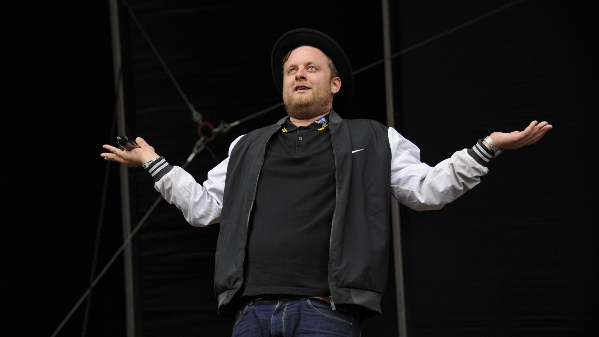 Der Rapper Fatoni steht beim Hurrican-Festival auf der Bühne. Er streckt seine Arme zur Seite und hat einen fragend-ironischen Blick. Der Rapper Fatoni steht beim Hurrican-Festival auf der Bühne. Er streckt seine Arme zur Seite und hat einen fragend-ironischen Blick.