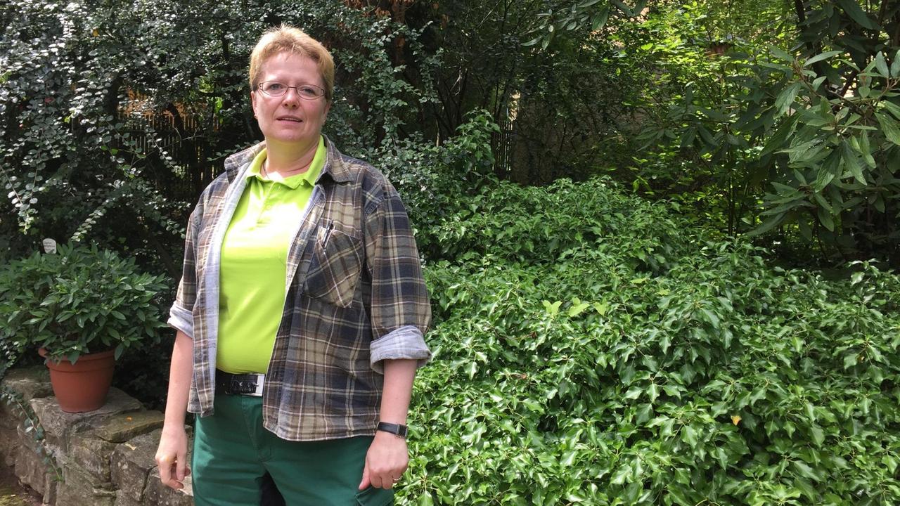 Organisatorin Simone Glaser, eine Frau in mittleren Jahren, gekleidet in Gärtner-Kleidung, im Botanischen Garten in Altenburg.