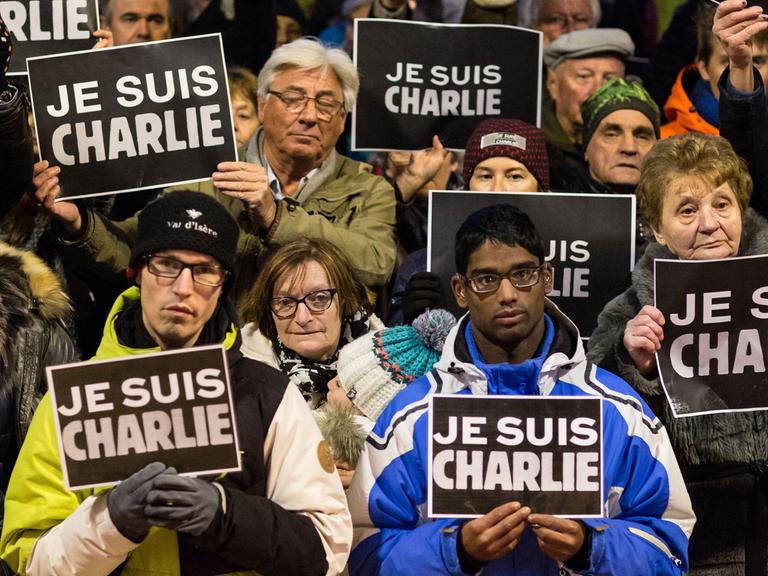 Menschen halten Schilder hoch, auf denen "Je suis Charlie" steht.