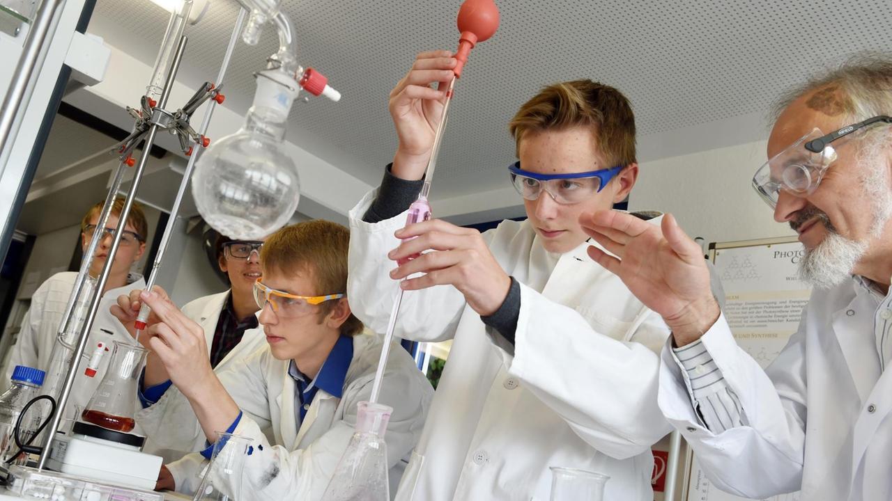 Der Forscher Rudolf Binder (r) beobachtet am 25.09.2015 im Schülerforschungszentrum Südwürttemberg in Bad Saulgau (Baden-Württemberg), wie Schüler Luca Braunger (Mitte) eine bestimmte Menge gefärbtes Wasser mit einer Pipette entnimmt.