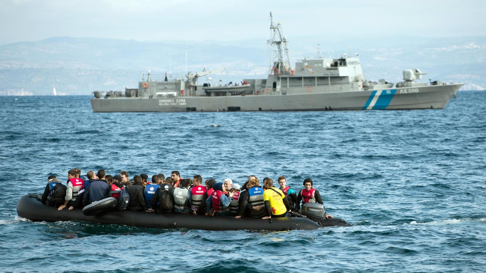Flüchtlinge fahren am 29.09.2015 mit einem Schlauchboot an einem Schiff der griechischen Küstenwache vorbei.