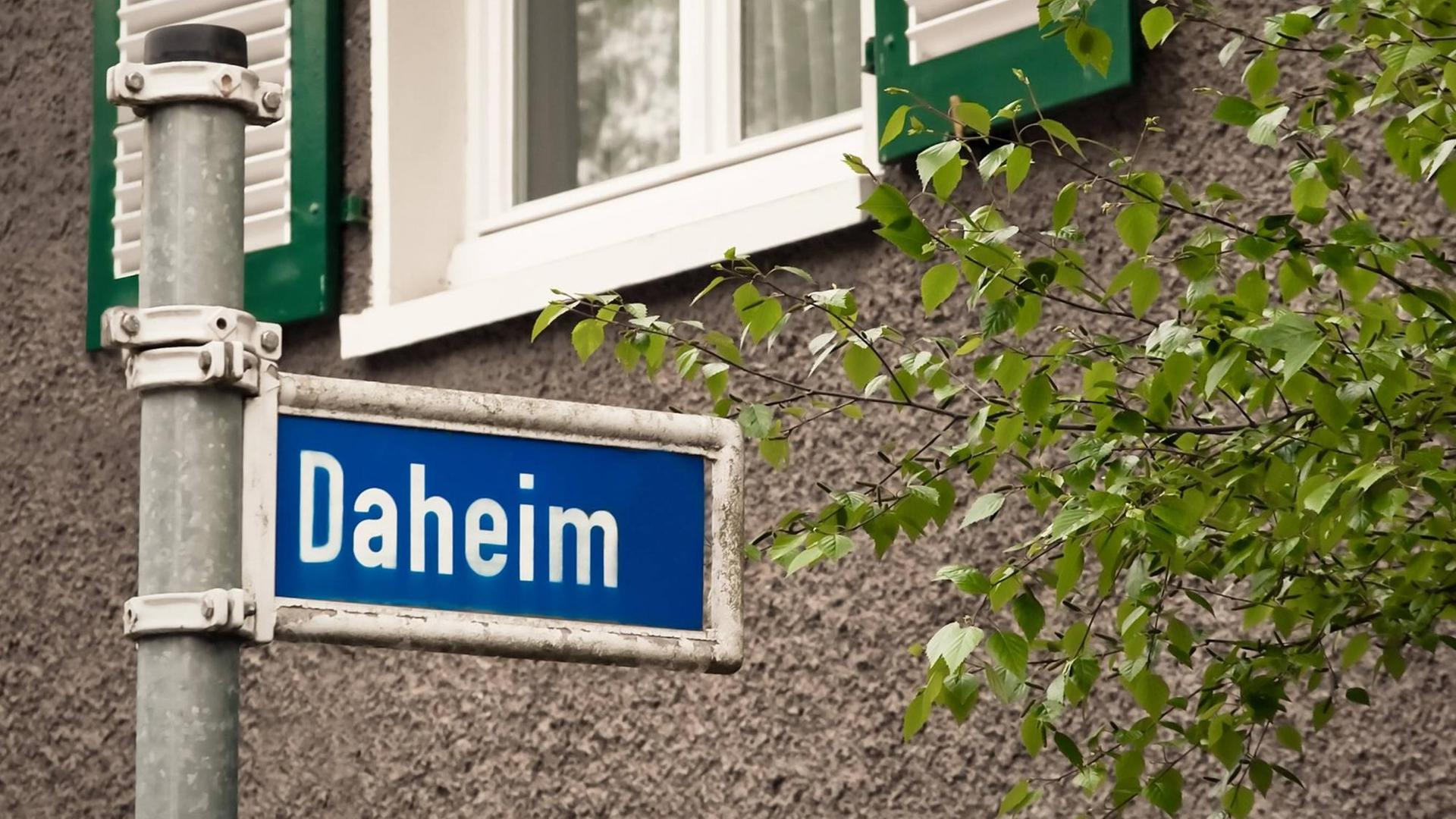 Ein blaues Straßenschild auf dem in weißen Buchstaben "Daheim" steht. Ein blaues Straßenschild auf dem in weißen Buchstaben "Daheim" steht.