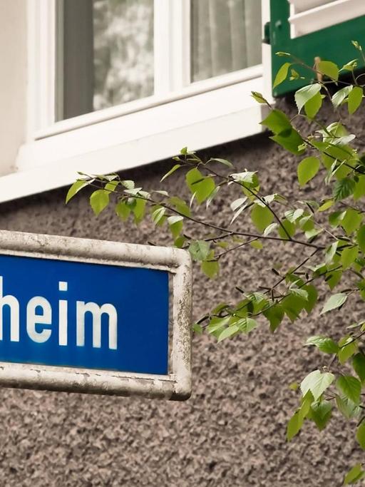Ein blaues Straßenschild auf dem in weißen Buchstaben "Daheim" steht.