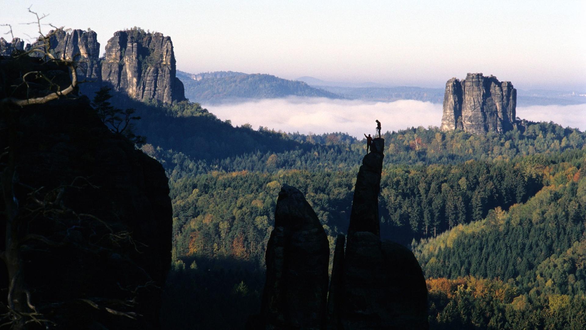 Zwei Bergsteiger auf dem Gipfel der Brosinnadel vor den Schrammsteinen (links) und dem Falkenstein im Nationalpark Sächsische Schweiz bei Bad Schandau. Zwei Bergsteiger auf dem Gipfel der Brosinnadel vor den Schrammsteinen (links) und dem Falkenstein im Nationalpark Sächsische Schweiz bei Bad Schandau.