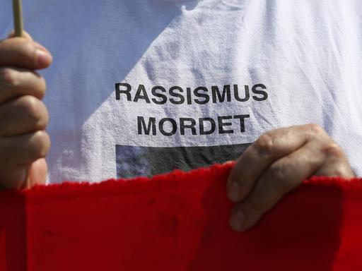 Der Schriftzug "Rassismus mordet" steht auf dem T-Shirt eines Demonstranten vor dem Reichstagsgebäude in Berlin. Mehrere Gruppen hatten am am 06.05.2013 zu einem Gedenken an die Opfer der NSU-Mordserie, als auch für alle anderen Opfer rechter Gewalt aufgerufen.