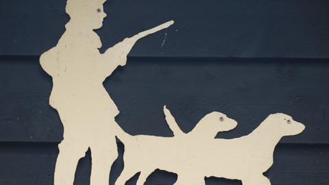 Auf einem Holzschnitt an einem Haus ist ein Jäger mit einem Gewehr und zwei Hunden zu sehen.