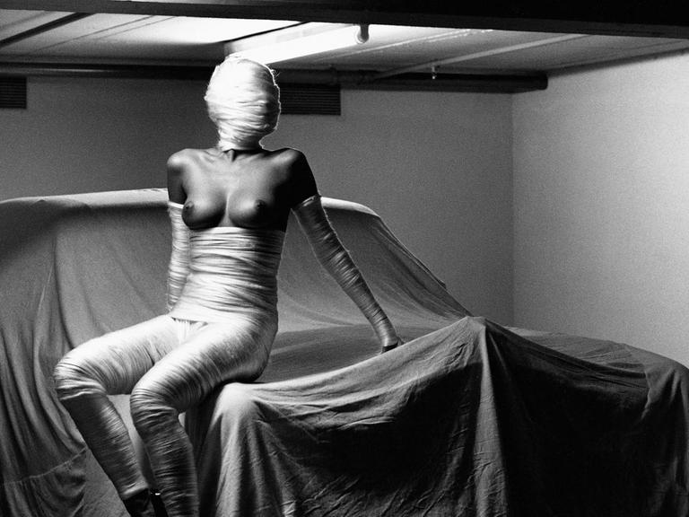 Zu sehen ist Newtons schwarz-weiß- Fotografie "In my Garage" als Teil der Ausstellung SUMO. Es zeigt einen Frauenkörper in freizügiger Pose auf einem mit Stoff eingehüllten PKW.