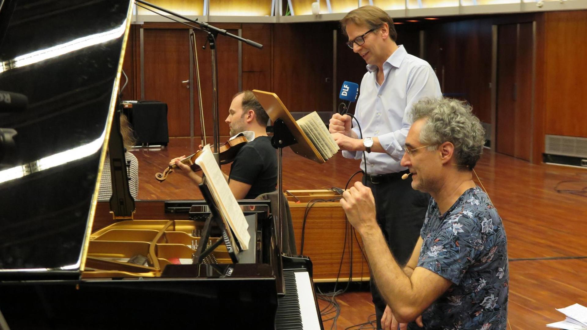 Ein Pianist sitzt am Flügel, dahinter Moderator und Geiger. Ein Pianist sitzt am Flügel, dahinter Moderator und Geiger.