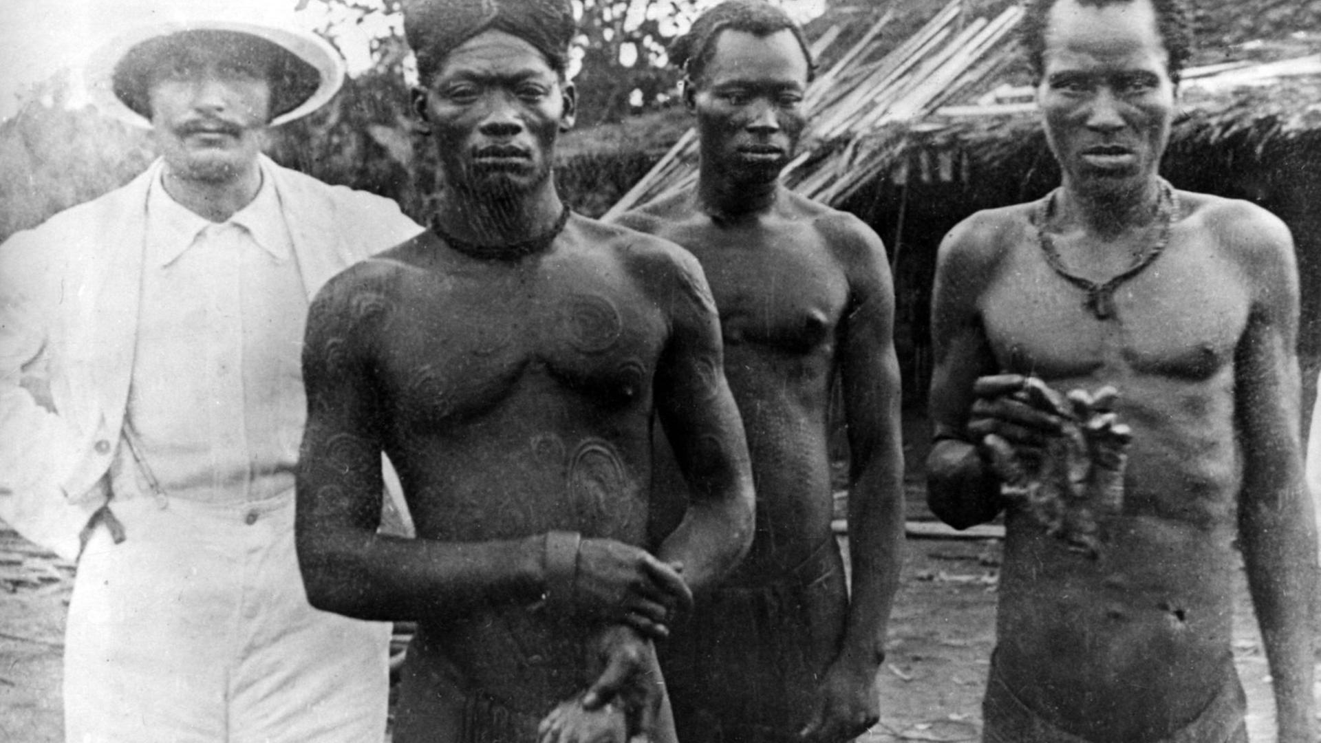 Ein Missionar mit kongolesischen Männern, die die amputierten Hände von zwei weiteren Männern zeigen (Lingomo and Bolenge), die als Kautschuk-Wachen von der ABIR (Anglo-Belgian India Rubber Company) beschäftigt waren. Demokratische Republik Kongo, Distrikt Nsongo. Foto von Alice Seeley Harris und ihrem Ehemann John Harris. Aufnahmedatum um 1904 geschätzt. Das Foto wurde verwendet, um den Roger Casement-Fall zu unterstützen. Roger Casement war ein britischer Diplomat, der entscheidend an der Aufklärung der Kongogräuel beteiligt war. Ein Missionar mit kongolesischen Männern, die die amputierten Hände von zwei weiteren Männern zeigen (Lingomo and Bolenge), die als Kautschuk-Wachen von der ABIR (Anglo-Belgian India Rubber Company) beschäftigt waren. Demokratische Republik Kongo, Distrikt Nsongo. Foto von Alice Seeley Harris und ihrem Ehemann John Harris. Aufnahmedatum um 1904 geschätzt. Das Foto wurde verwendet, um den Roger Casement-Fall zu unterstützen. Roger Casement war ein britischer Diplomat, der entscheidend an der Aufklärung der Kongogräuel beteiligt war.