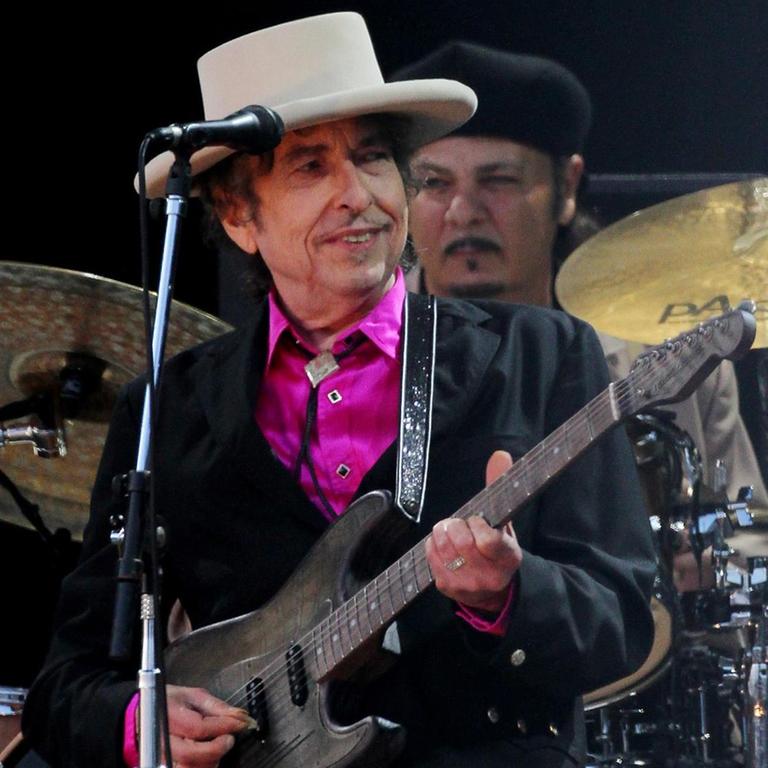 Der Sänger Bob Dylan bei einem Auftritt. Er trägt einen hellen Hut und ein pinkfarbenes Hemd.